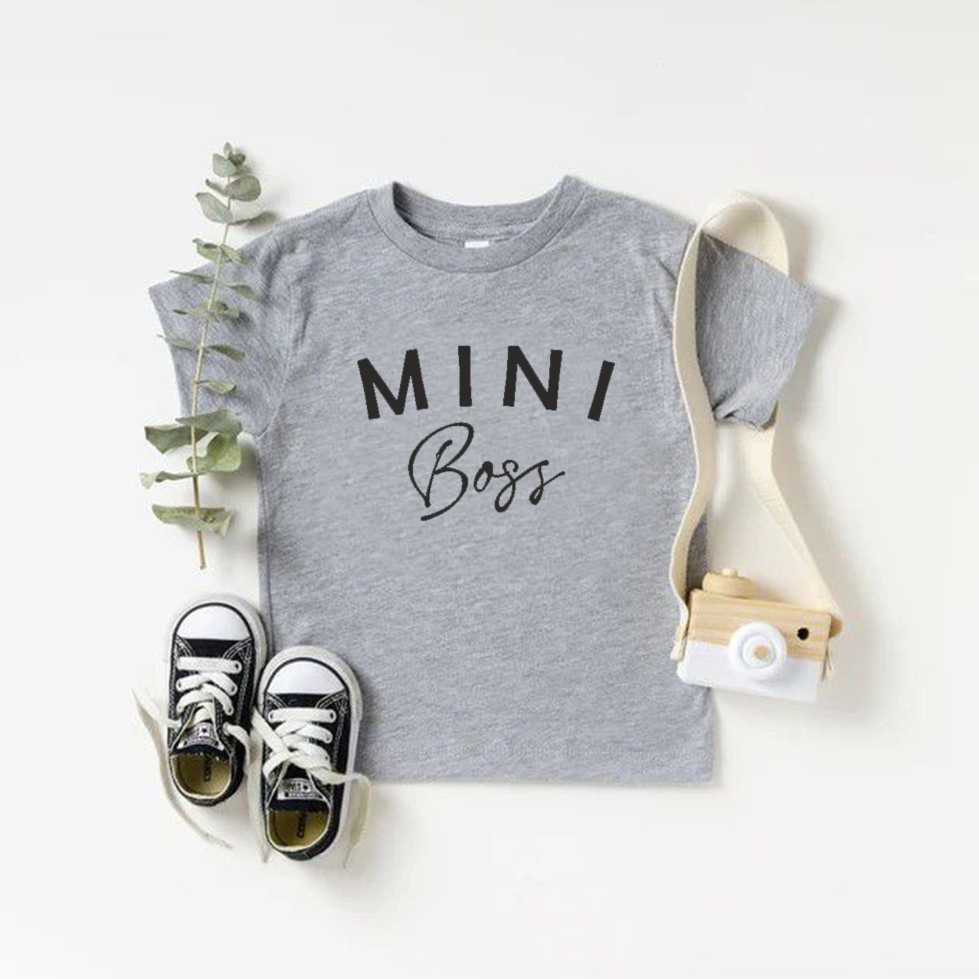 Gray t-shirt with 'MINI Boss' text, black sneakers, and a small bag on a white background