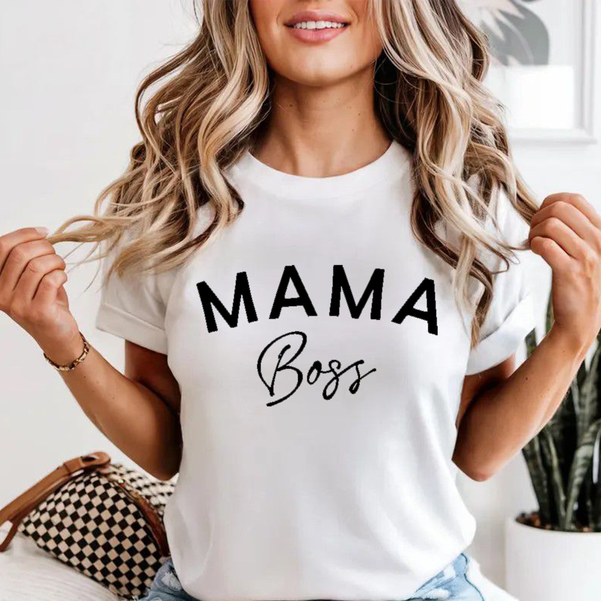 Woman wearing a white t-shirt with 'MAMA Boss' text, sitting indoors.